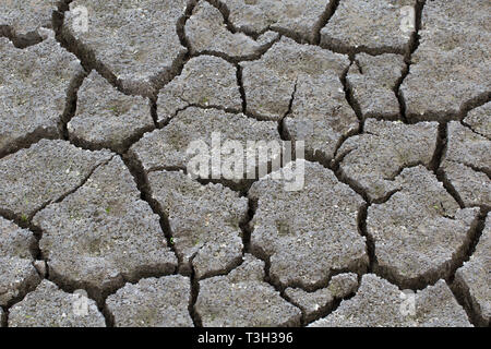 Abstract pattern of dry cracked clay mud in dried up lake bed / riverbed caused by prolonged drought in summer in hot weather temperatures Stock Photo