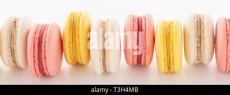 Pink, yellow and white macarons in a row on white background. Banner. Stock Photo