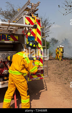 Sierra Leoneans in emergency response team training in fire fighting  make fire breaks between local woodland and community using hoses from tenders Stock Photo