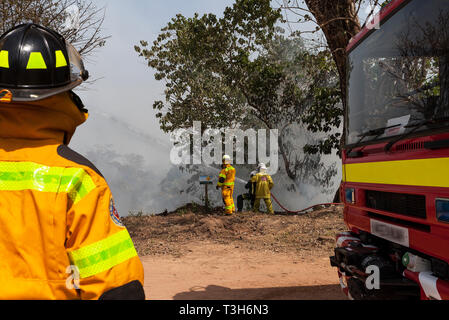 Sierra Leoneans in emergency response team training in fire fighting  make fire breaks between local woodland and community using hoses from tenders Stock Photo