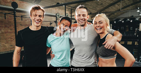Laughing group of diverse friends in sportswear standing arm in arm after working out together at the gym Stock Photo