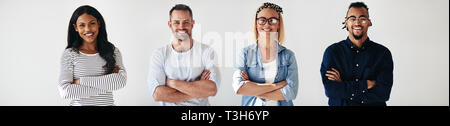 Smiling group of diverse young entrepreneurs standing in a row with their arms crossed against a white background Stock Photo
