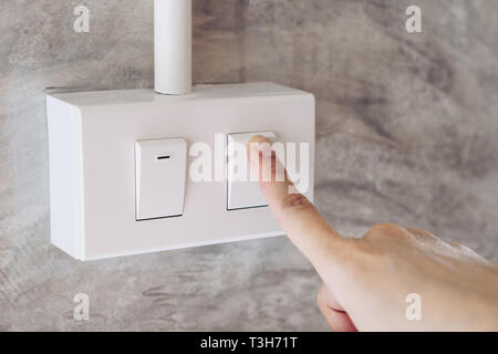 Women hand turn on lights electric switch on cement wall background Stock Photo