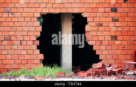 Broken red  brick wall with a big hole and a construction column pillar in the middle Stock Photo