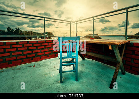 Retro wooden blue chair and a wooden table on the balcony with red brick walls and a moody atmosphere. Stock Photo