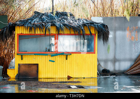 Small yellow wooden hut with red window frames and a thatched roof on a wet rainy day Stock Photo