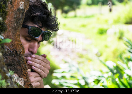 Young man lighting a cigar behind a tree in a forest. Stock Photo