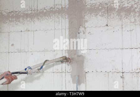 Builder hold in hands automatic cement wall screeding plaster machine.  Plastering wall with spray plastering  machine for house plastering walls. Stock Photo