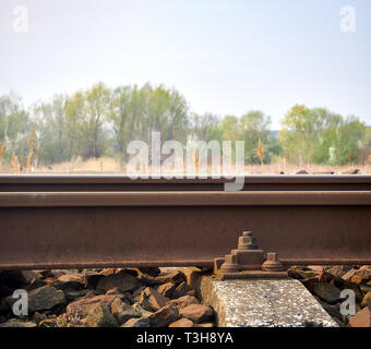 Close-up view of rails with concrete fret with screw. Blurred landscape with forest on background. Stock Photo