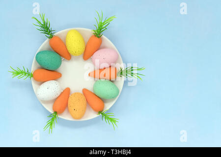 Colourful Easter eggs and carrots on a white saucer, on a light blue background with copy space Stock Photo