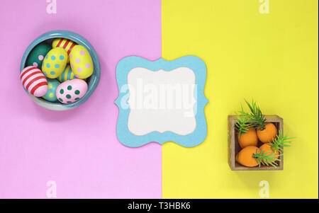 Easter eggs and carrots on a pink and yellow background, with a copy space in the centre and a blue frame Stock Photo