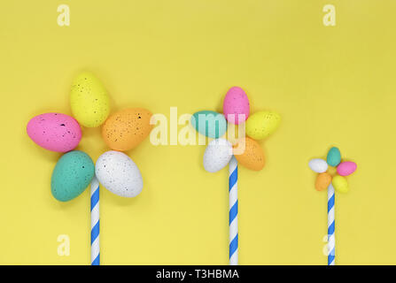 Three flowers made from colourful easter eggs. Flat lay against a yellow background, with space for copy. Stock Photo