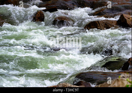 Cascading river water flows over rocks in the river creating rapids. Stock Photo