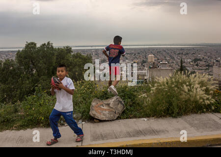 Two young boys play football, in front of a view of the city of Chimalhuac‡n, the State of Mexico, Mexico, and Lake Texcoco in the background on August 25, 2017. The new Mexico City International Airport is being constructed on the other side of Lake Texcoco. Mexico's newly elected president Andreas Lopez Manuel Obrador cancelled this project in the fall of 2018, while it was in the middle of construction. The airport was set to replace the aging Benito Juarez International Airport. Stock Photo