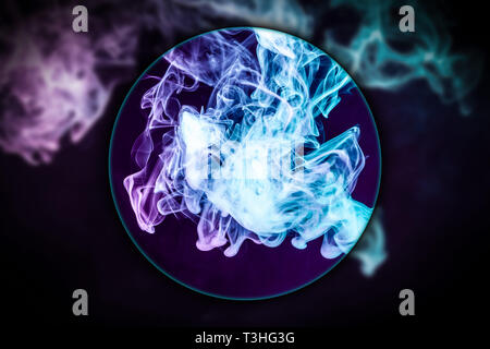 Close-up pink and blue cloud of smoke   blown under a magnifying glass on  black isolated background. Background from the smoke of vape Stock Photo