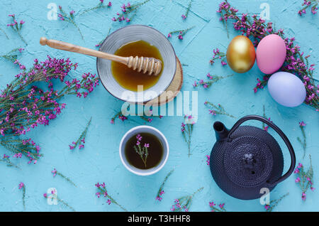 Tea with honey, easter eggs and purple heather flowers on blue background. Flat lay. Stock Photo