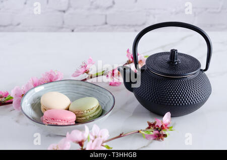 Black teapot and macaroni with peach flowers on marble background. Stock Photo