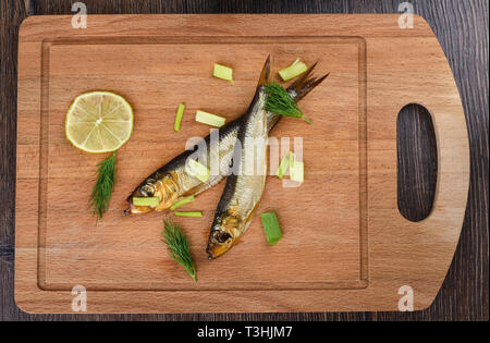 Two baltic herrings cold smoked with dill, green onions and lime on a wooden cutting board. Two aromatic baltic herrings smoked until golden. Close up Stock Photo