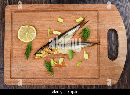 Two baltic herrings cold smoked with dill, green onions and lime on a wooden cutting board. Two aromatic baltic herrings smoked until golden. Close up Stock Photo
