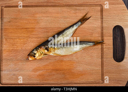 Two baltic herrings cold smoked on a wooden cutting board. Two aromatic baltic herrings smoked until golden. Close up Stock Photo