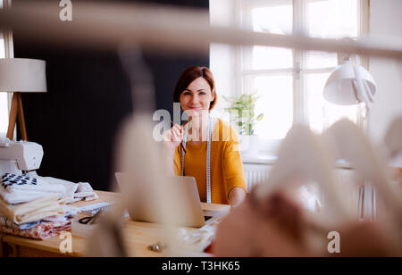 Young creative woman in a studio, using laptop. A startup of tailoring business. Stock Photo