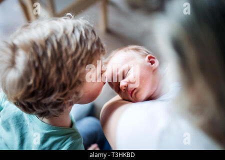 A small boy kissing a sleeping newborn baby brother at home.