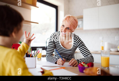 A young woman with small daughter drawing in a kitchen. Stock Photo