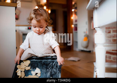 A small toddler girl making cakes on the floor in the kitchen at home. Stock Photo