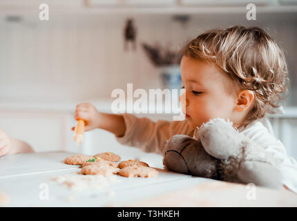 A small toddler girl sitting at the table, decorating cakes at home. Stock Photo