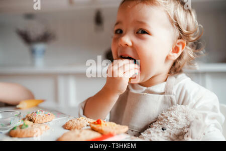 A small toddler girl sitting at the table, decorating cakes at home. Stock Photo