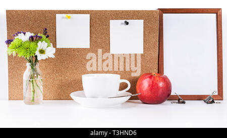 MockUp. Empty frame, corkboard with two clean white stickers pinned to it. White cup, red apple and a small bouquet of flowers. White Desktop Concept Stock Photo
