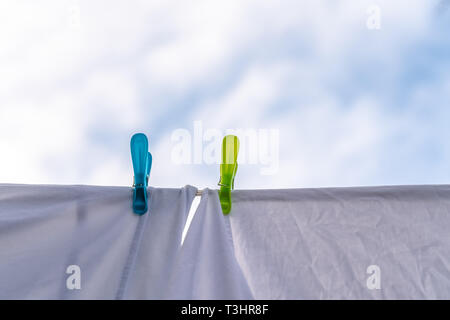 White clothes hung out to dry on a washing line and fastened by the clothes pegs against the blue sky in the bright warm sunny day Stock Photo