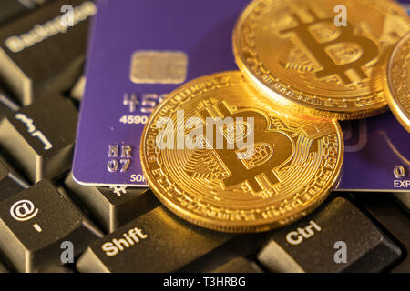 Two gold bitcoins with a blue credit card on top of computer keyboard at the background, cryptocurrency accepting for payment and finance concept Stock Photo