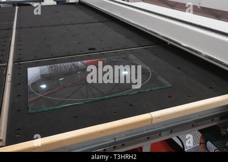 piece of transparent glass lays on industrial CNC computer remote controlled glass cutter water-jet or laser system Stock Photo