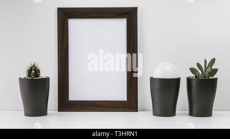 Empty dark photo frame, two succulents in dark pots and a white light bulb on a white background. Scandinavian style in the interior. Stock Photo