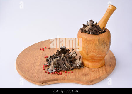 Dried edible, aromatic  Horn on plenty mushrooms in bamboo wooden mortar, on bamboo chopping board, over white Stock Photo
