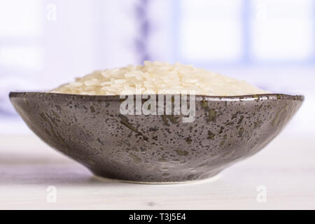 Lot of whole white jasmine rice grains on grey ceramic plate with blue window in a white kitchen