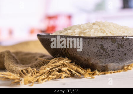 Lot of whole white jasmine rice grains on grey ceramic plate on jute cloth in a white kitchen