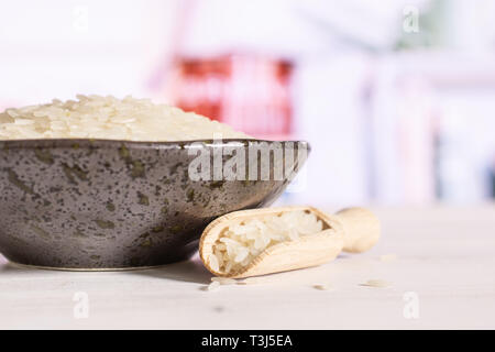 Lot of whole white jasmine rice grains on grey ceramic plate with wooden scoop in a white kitchen