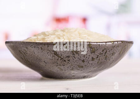 Lot of whole white jasmine rice grains on grey ceramic plate in a white kitchen