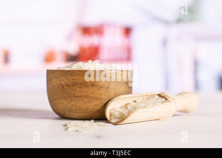 Lot of whole white jasmine rice grains in a wooden bowl with wooden scoop in a white kitchen