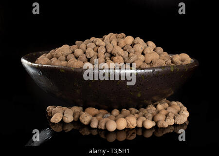 Lot of whole brown clay pebbles (leca) on grey ceramic plate isolated on black glass Stock Photo