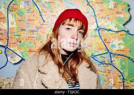 Girl, teenager, with a red beanie and headphones in her ear standing in front of a city map at night, Cologne, North Rhine-Westphalia, Germany Stock Photo