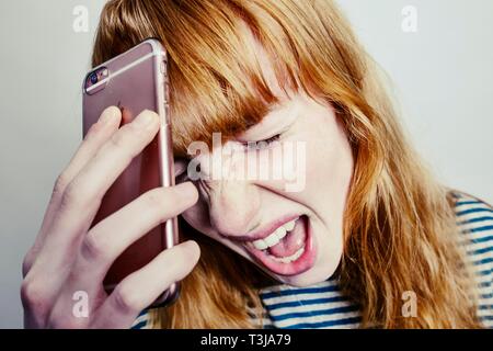 Girl, teenager, red-haired, holding her head in despair screaming smartphone, studio shot, Germany Stock Photo