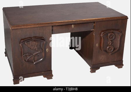A writing desk belonging to Oberarbeitsführer (Senior Work Leader), Wilhelm Krach Arbeitsgau (Work District) 24, Middle Rhine, Koblenz Dark brown stained oak(?) with two side cupboards, three interior drawers and a central drawer. Four cartouches carved as coats of arms in high relief - those in front bearing a head of grain and a spade in a wreath of grain on a swastika (emblem for RAD - Distinguished Service) or a spade with a swastika above heads of grain (banner emblem). The two cupboard doors in back display the civic coats of arms for Krach's previous postings, Mainz , Editorial-Use-Only Stock Photo