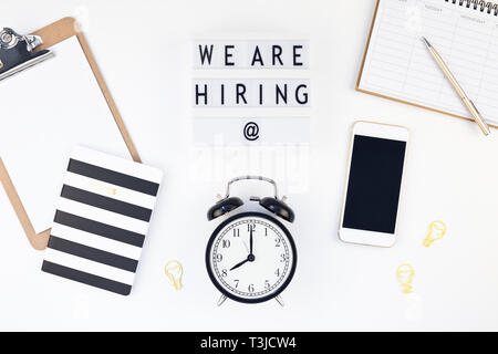 Creative top view flat lay of desk with we are hiring text on lightbox with copy space on white background in minimal style. Concept of new job, hirin Stock Photo