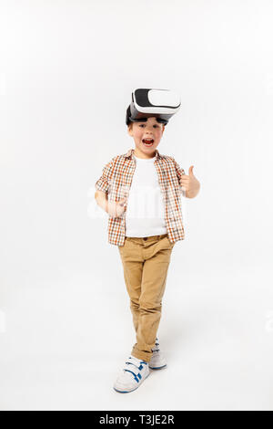 Happy and wondering. Little boy or child in jeans and shirt with virtual reality headset glasses isolated on white studio background. Concept of cutting edge technology, video games, innovation. Stock Photo