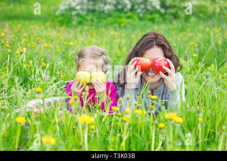 Mother and daughter on sunny meadow with apples in hands Stock Photo