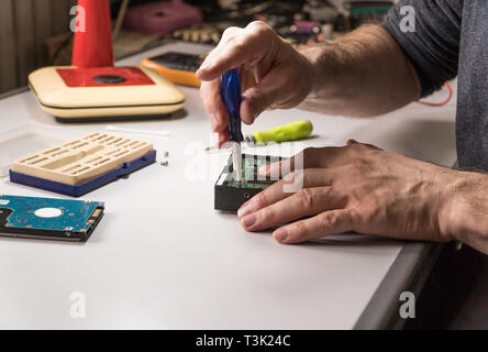 electronic engineer repairs computer hard drive. technologist with a screwdriver disassembles hdd Stock Photo