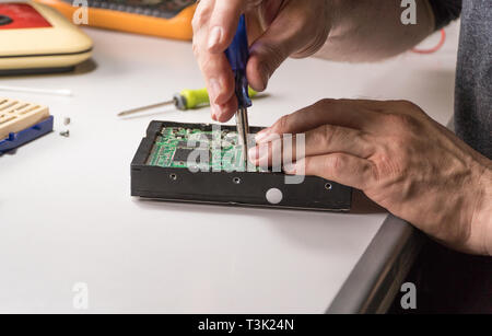 electronic engineer repairs computer hard drive. technologist with a screwdriver disassembles hdd Stock Photo